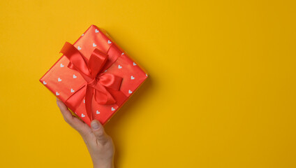 Two female hands hold a box wrapped in red paper and tied with a red silk ribbon, holiday