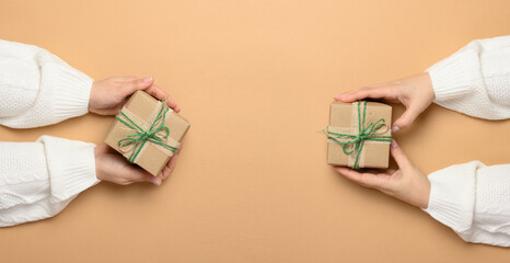 Female hands holding a gift box on a beige background. View from above