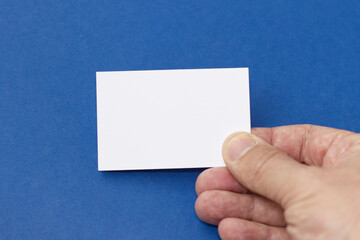 Hand of man holding paper card isolated on blue background, business card showing.