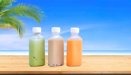 Iced Bubble milk tea with green milk tea and cold Ovomaltine in transparent plastic bottles on wooden table with blurred sea view background, summer refreshing drink