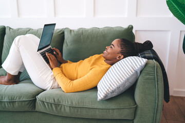 Black man using laptop and lying on sofa