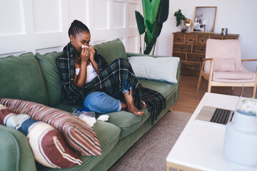 Obraz premium Ethnic unhealthy woman with tissue paper sitting on couch in living room