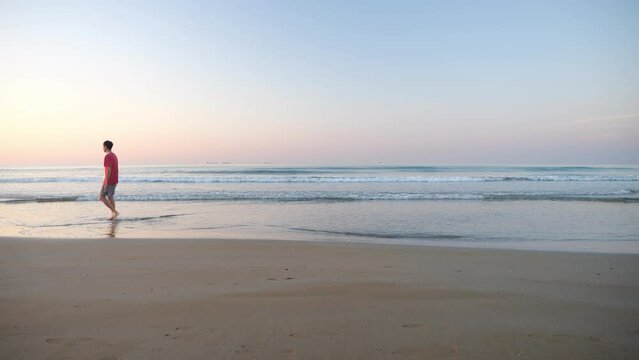 A young man walks on the shoreline with his feet in the sea water early in the morning