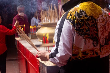 Chinese people celebrating traditional Chinese New Year in Chinese temple, they burning incense and praying, holiday concept - obrazy, fototapety, plakaty