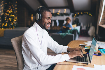 Adult Black male, enjoys music on headphones while working on a laptop in a home setting with...