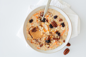 Carrot cake oatmeal with dried cranberries, pecans and peanut butter in white plate, white background. Healthy winter breakfast concept.