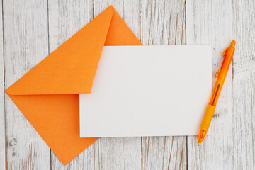 Blank greeting card with orange envelope and pen on wood