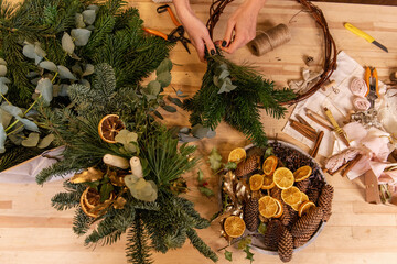 Top view composition of female hands making Christmas wreath from natural branches of spruce, pine,...
