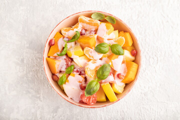 Vegetarian fruit salad of yogurt pumpkin, tangerine, basil microgreen on gray, top view, close up.