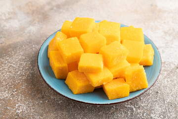 Dried mango cubes on blue plate on brown concrete, side view.