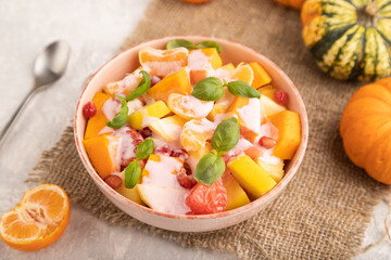 Vegetarian fruit salad of yogurt pumpkin, tangerine, basil microgreen on gray, side view, selective focus.