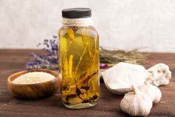 Sunflower oil in a glass jar with various herbs and spices on a brown wooden. Side view.