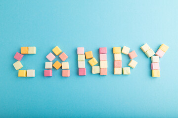 The inscription "candy" laid out with fruit chewing candies on blue pastel, top view, copy space