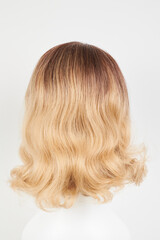 Naklejka premium Natural looking blonde fair wig on white mannequin head. Middle length hair cut on the plastic wig holder isolated on white background, back view