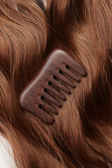 Curls of brown hair and a wooden comb on a white background, hair care, beauty salon concept