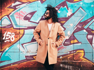 Handsome hipster model. Arabian man dressed in brown coat clothes. Fashion male with long curly hairstyle posing outdoors in street. Cheerful and happy