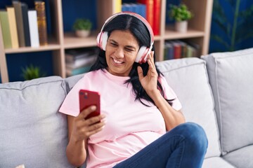 Middle age hispanic woman listening to music sitting on sofa at home
