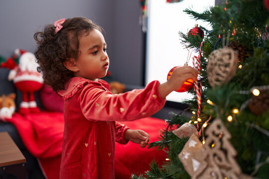 Adorable hispanic girl decorating christmas tree at home