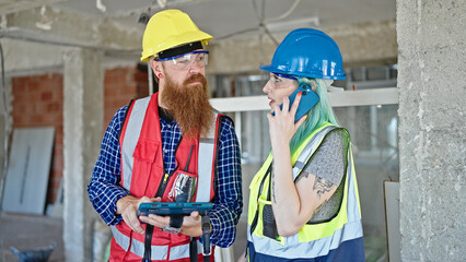 Man and woman builders talking on smartphone using touchpad at construction site