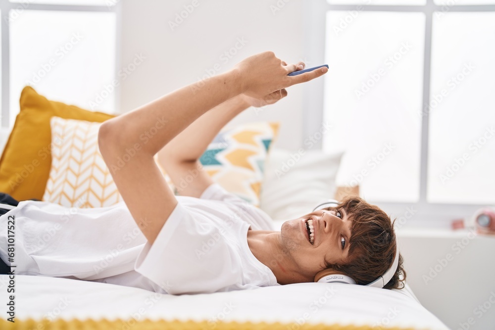 Poster Young blond man listening to music lying on bed at bedroom