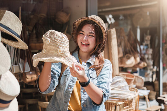 Asian tourist girl shopping, walking in famous local street market looking at beautiful straw hats, happy shopping at local market on weekend.