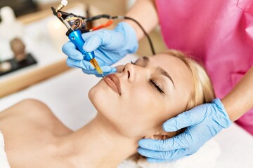 Obraz na płótnie Canvas Young caucasian woman lying on table having microblading treatment at beauty salon