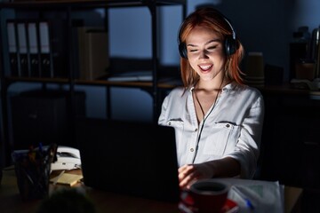 Young caucasian woman working at the office at night winking looking at the camera with sexy...
