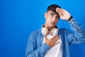 Young hispanic man standing over blue background touching forehead for illness and fever, flu and cold, virus sick
