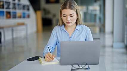 Young blonde woman business worker using laptop taking notes at office