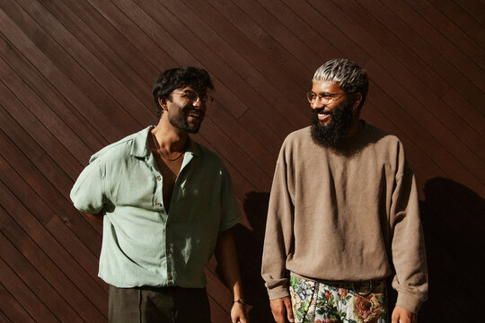 Two young multiracial friends in trendy clothes having fun in front of brown wall