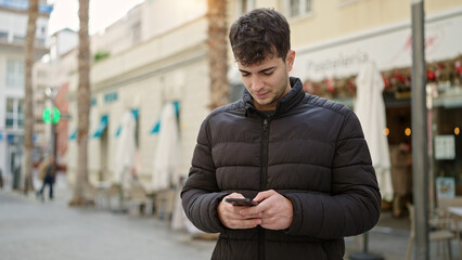 Young hispanic man using smartphone at coffee shop terrace