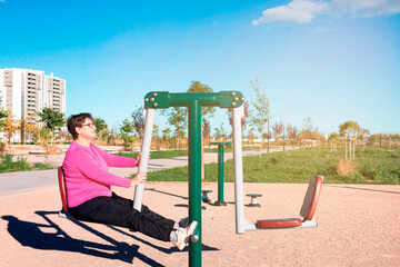 Mature woman exercising her legs on a fitness machine in the street.