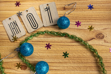 Wooden Christmas background with text January 1st. Nearby are decorative Christmas tree toys, snowflakes and small tinsel for interior decoration. Background image for postcards or presentations.