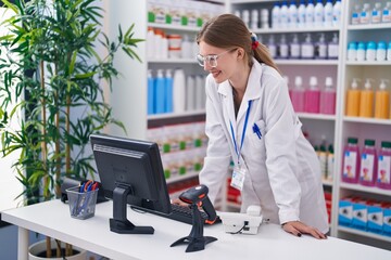 Young blonde woman pharmacist smiling confident using computer at pharmacy