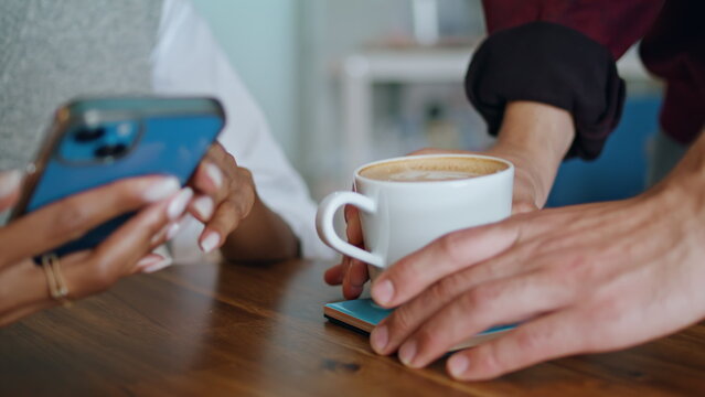 Barista putting cup coffee on table to woman sitting with smartphone closeup. - Powered by Adobe
