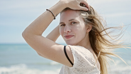 Young blonde woman tourist smiling confident touching hair at beach