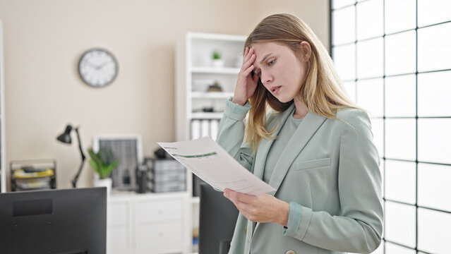Young blonde woman business worker reading document with worried expression at office