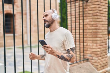 Young bald man listening to music and dancing with serious expression at street