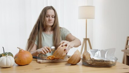 Young Woman with Long Hair Cleans Seeds from a Small Pumpkin, Other Pumpkins of Various Colors Lie on the Table. Circular Motion.