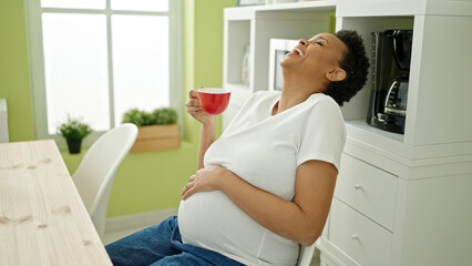 Young pregnant woman drinking coffee sitting on table at dinning room