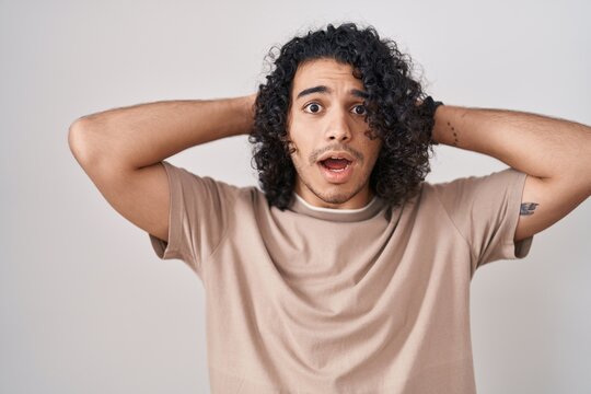 Hispanic man with curly hair standing over white background crazy and scared with hands on head, afraid and surprised of shock with open mouth