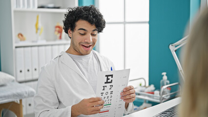 Young latin man optician examining vision with snellen test at clinic