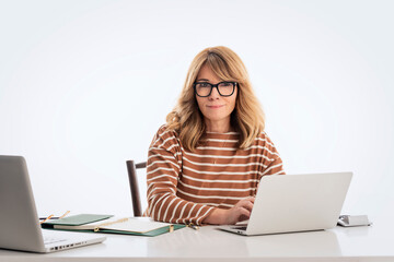 Mid aged businesswoman sitting at desk and using laptops against isolated white backgroung