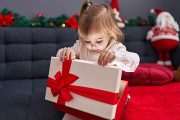 Fototapeta na wymiar Adorable blonde girl unpacking gift sitting on sofa by christmas decor at home