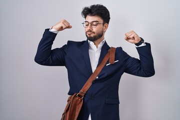 Hispanic man with beard wearing business clothes showing arms muscles smiling proud. fitness concept.