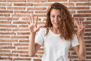 Young caucasian woman standing over bricks wall background showing and pointing up with fingers...