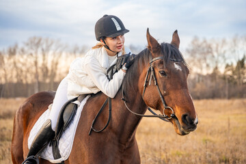 Obraz premium Beautiful blond professional female jockey riding a horse. Friendship with horse.