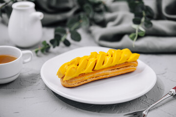 Fresh tasty eclair on white plate and cup of tea