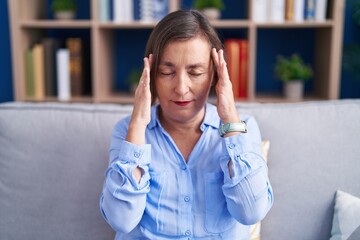Fototapeta premium Middle age hispanic woman sitting on the sofa at home with hand on head for pain in head because stress. suffering migraine.