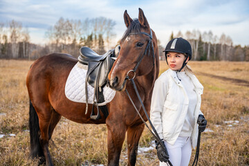 Fototapeta premium Blond professional female jockey standing near brown horse in field. Friendship with horse